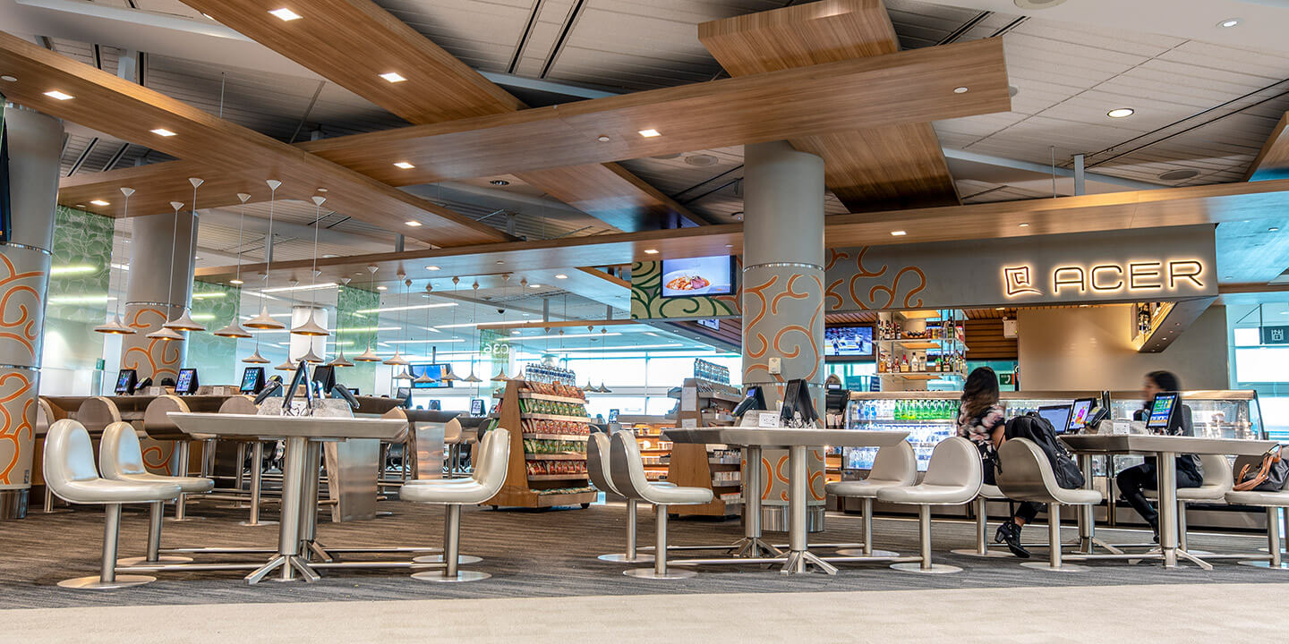 Enseigne Acer allumé au-dessus du restaurant ouvert avec des tables et des chaises beiges