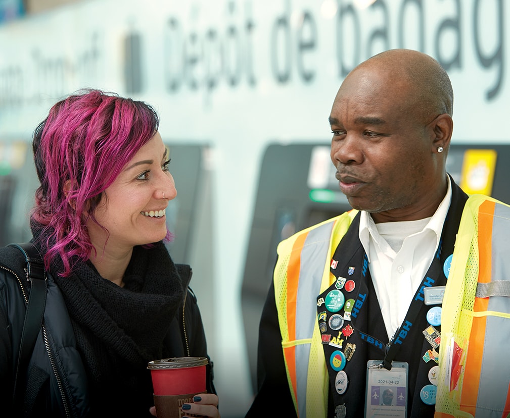 A traveller and an employee smile while interacting in a Toronto Pearson baggage area