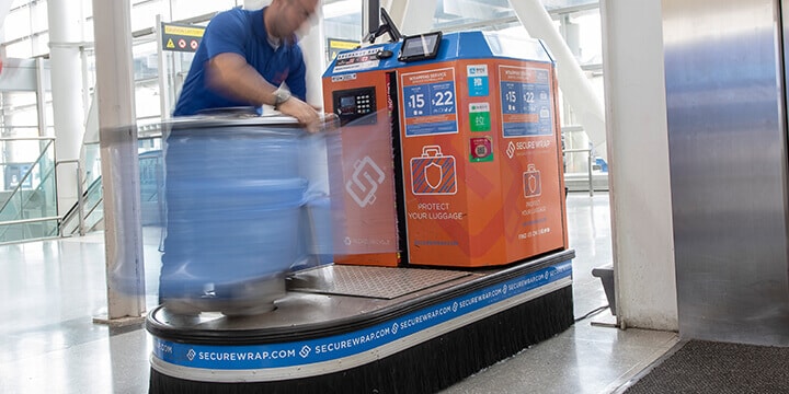 Un homme emballe des bagages dans des feuilles de plastique bleu sur une machine Secure Wrap 